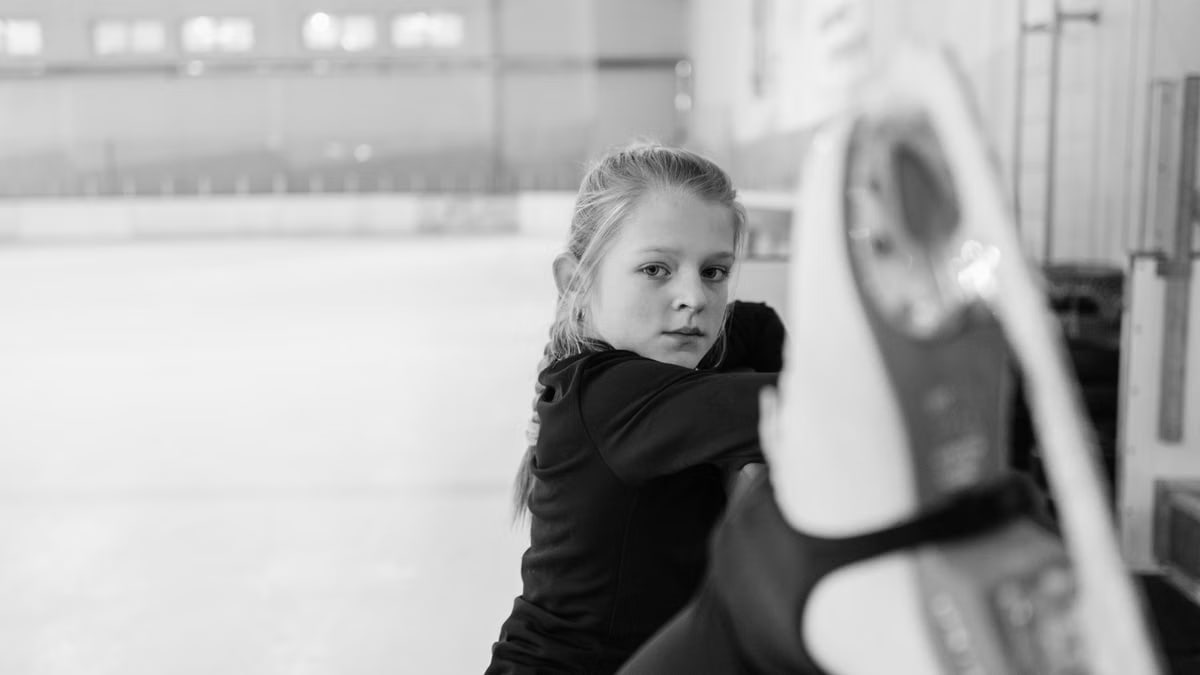 A focused girl practicing figure skating on an indoor ice rink in monochrome.